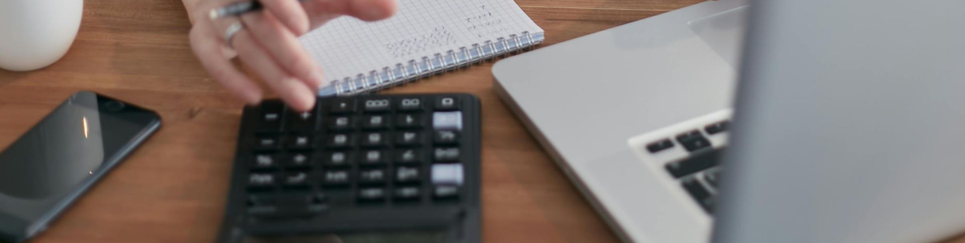 Adult woman working on finances using a laptop and calculator on a wooden table indoors.