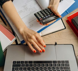 A business professional uses a calculator among documents and laptop on a desk for financial tasks.